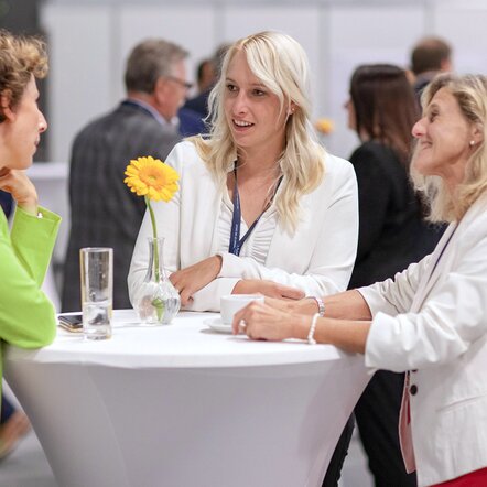 Drei Frauen reden an einem Stehtisch miteinander